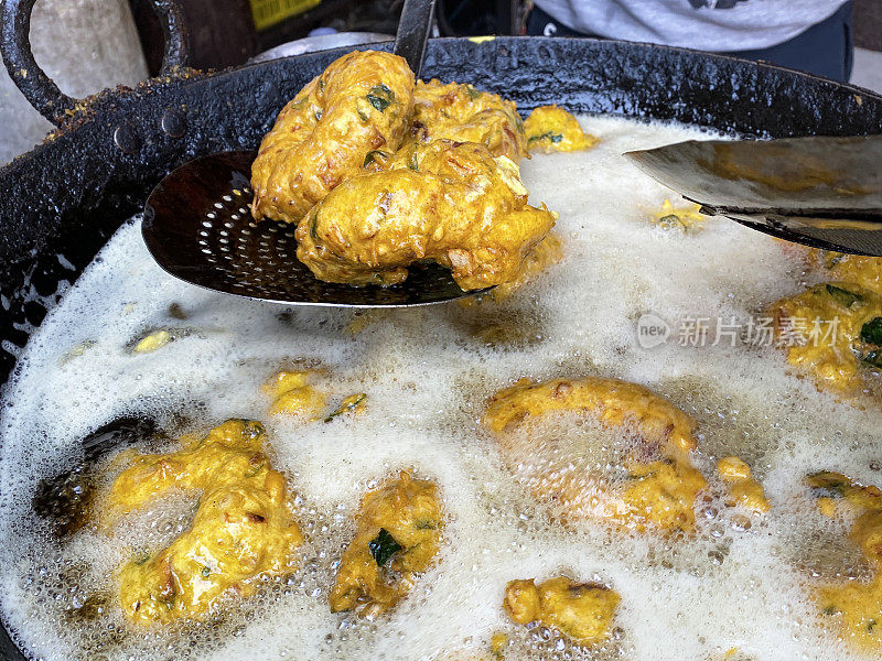 金黄色的Medu vada(软油条)早餐小吃，户外炉子上的街头小吃，厨师用开槽的勺子转动由Vigna mungo(黑扁豆)制成的美味甜甜圈，油炸锅里的油沸腾，前景的高度聚焦